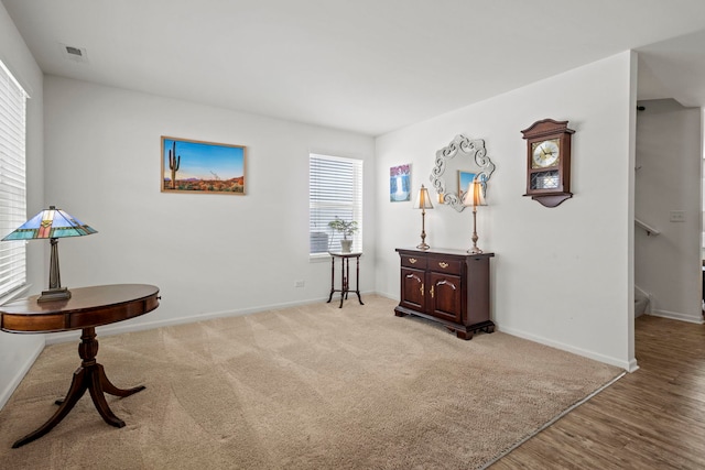 living area featuring visible vents, baseboards, light colored carpet, light wood-style flooring, and stairway