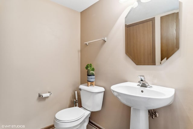 half bath featuring baseboards and toilet