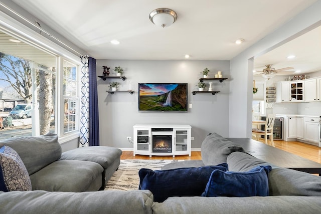 living room featuring beverage cooler, baseboards, a glass covered fireplace, light wood-style flooring, and recessed lighting