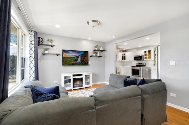 living area featuring a glass covered fireplace, baseboards, light wood finished floors, and recessed lighting