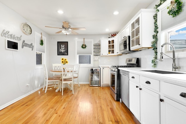 kitchen featuring beverage cooler, a sink, white cabinetry, light countertops, and appliances with stainless steel finishes