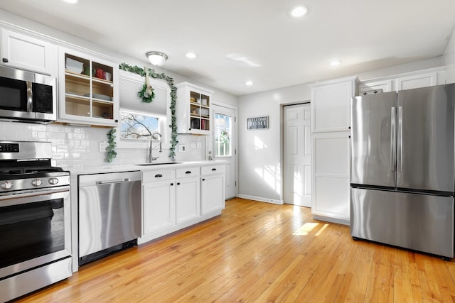 kitchen featuring a sink, white cabinetry, light countertops, appliances with stainless steel finishes, and glass insert cabinets