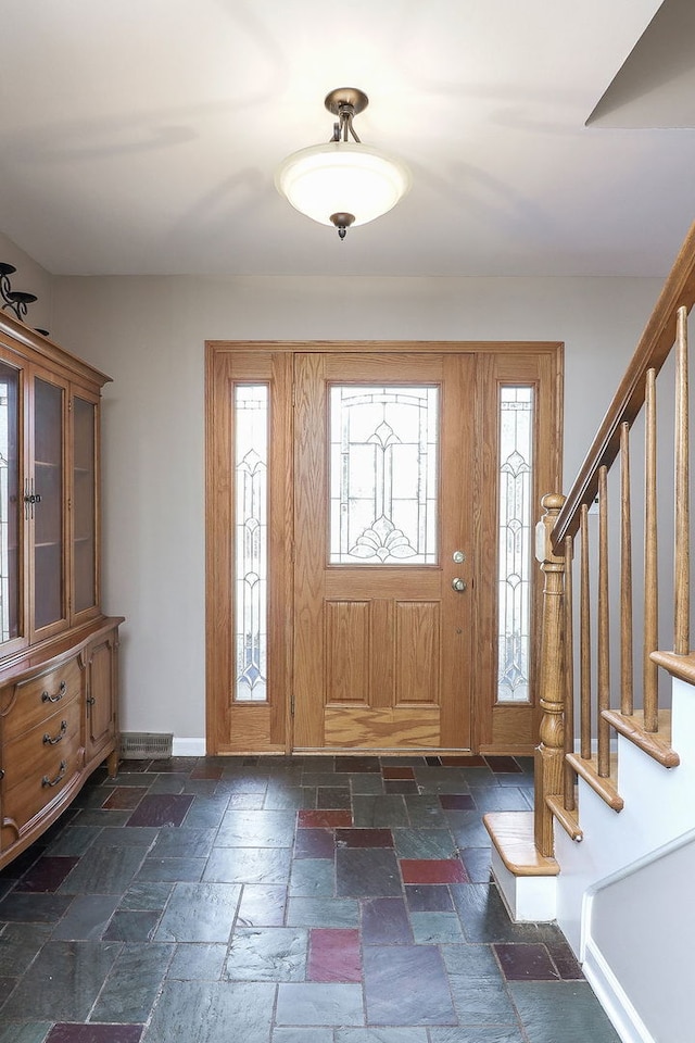 foyer featuring baseboards, stairway, and stone tile floors