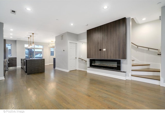 unfurnished living room with dark wood-type flooring, a glass covered fireplace, stairway, and recessed lighting