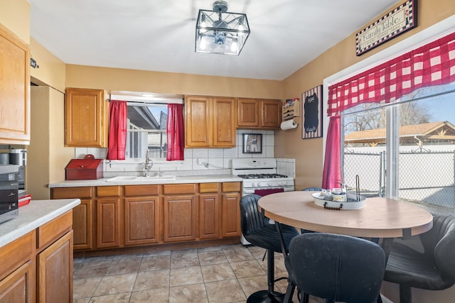 kitchen featuring white gas stove, a sink, light countertops, brown cabinets, and tasteful backsplash