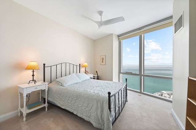 carpeted bedroom with visible vents, expansive windows, baseboards, and a water view