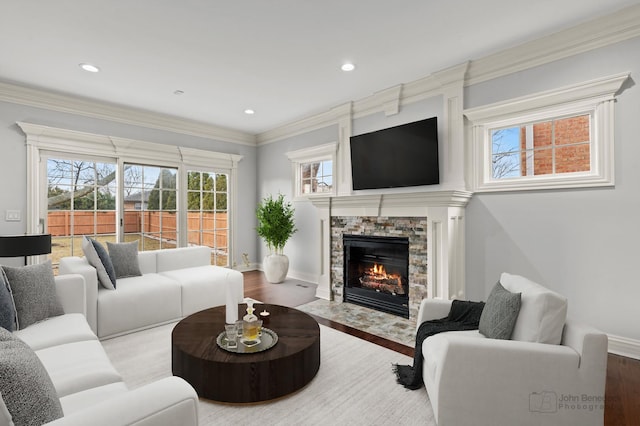 living area with ornamental molding, a stone fireplace, baseboards, and wood finished floors