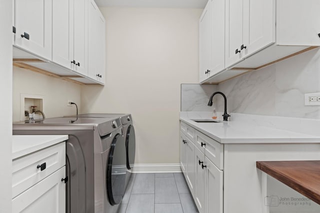 laundry room featuring cabinet space, light tile patterned floors, baseboards, washing machine and dryer, and a sink