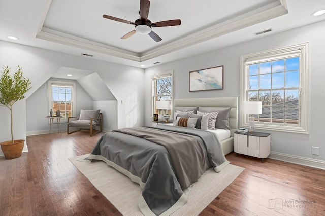 bedroom with baseboards, visible vents, a raised ceiling, and wood finished floors