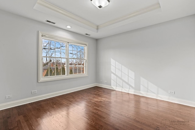 spare room featuring baseboards, visible vents, dark wood-type flooring, a tray ceiling, and crown molding