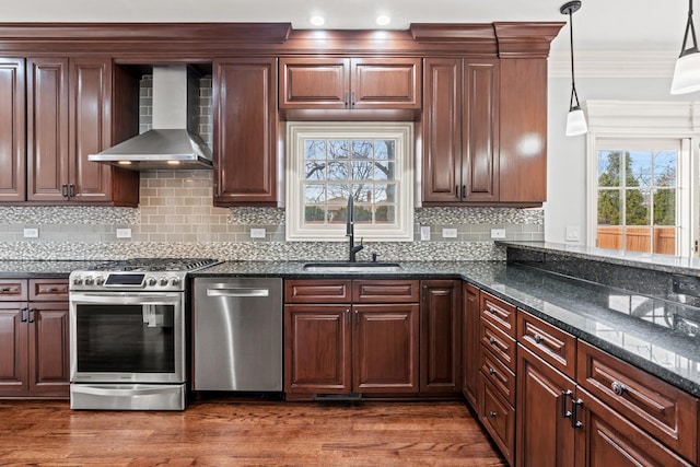 kitchen with appliances with stainless steel finishes, ornamental molding, a sink, wood finished floors, and wall chimney exhaust hood