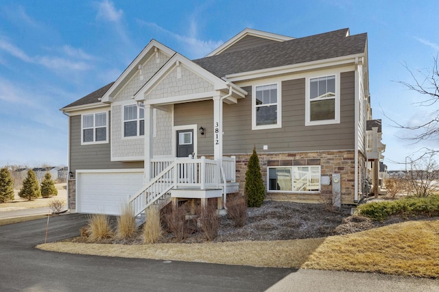 raised ranch with a garage, stone siding, driveway, and a shingled roof