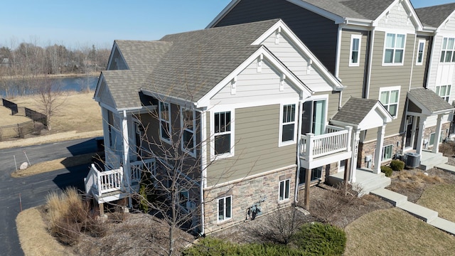 view of side of home with stone siding, roof with shingles, central AC, and a water view