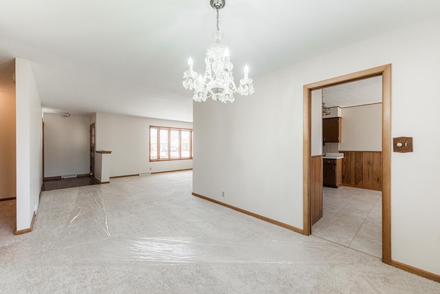 spare room featuring a notable chandelier, baseboards, and light colored carpet