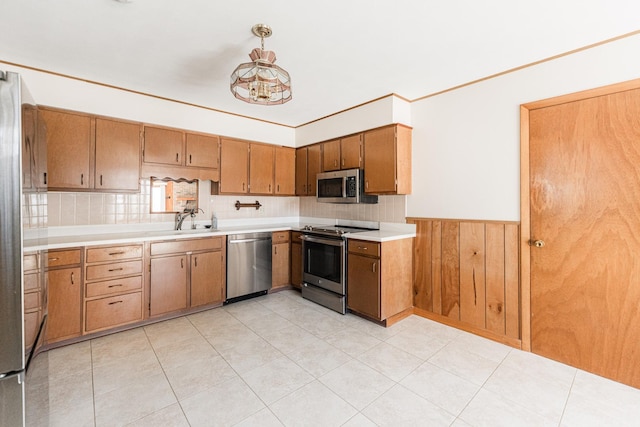 kitchen with appliances with stainless steel finishes, light countertops, wainscoting, and a sink