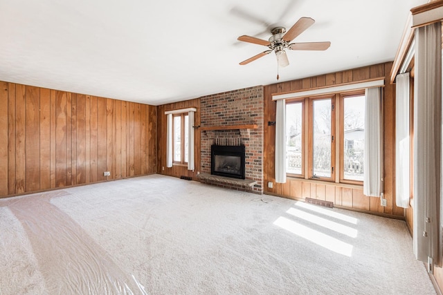 unfurnished living room with wooden walls, visible vents, a ceiling fan, carpet floors, and a brick fireplace