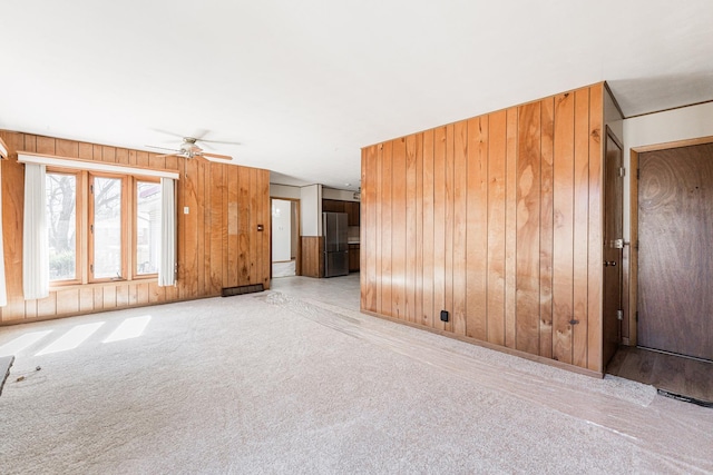 carpeted empty room featuring wood walls and a ceiling fan