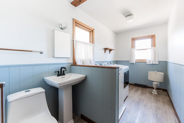 half bathroom featuring visible vents, toilet, a wainscoted wall, wood finished floors, and a sink