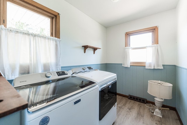 laundry area with a wainscoted wall, laundry area, washing machine and dryer, and light wood-style flooring