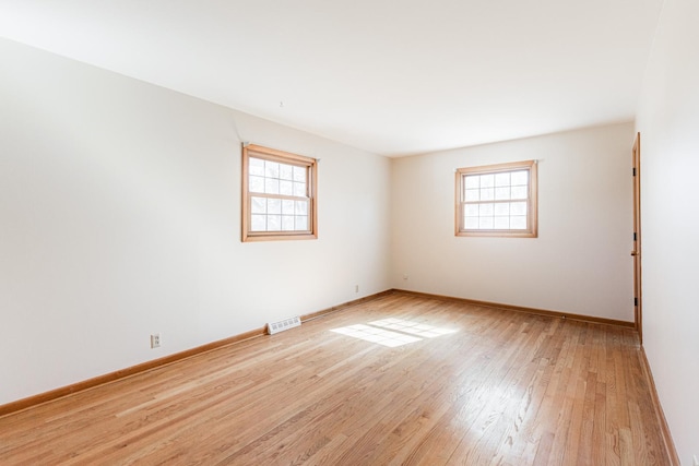 empty room featuring a wealth of natural light, baseboards, visible vents, and light wood finished floors