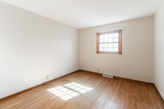 empty room with hardwood / wood-style flooring, baseboards, and visible vents