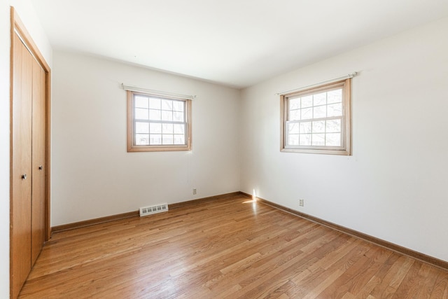 unfurnished bedroom with a closet, light wood-type flooring, visible vents, and baseboards