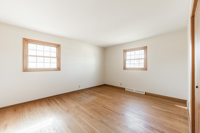 spare room featuring light wood finished floors, visible vents, and baseboards