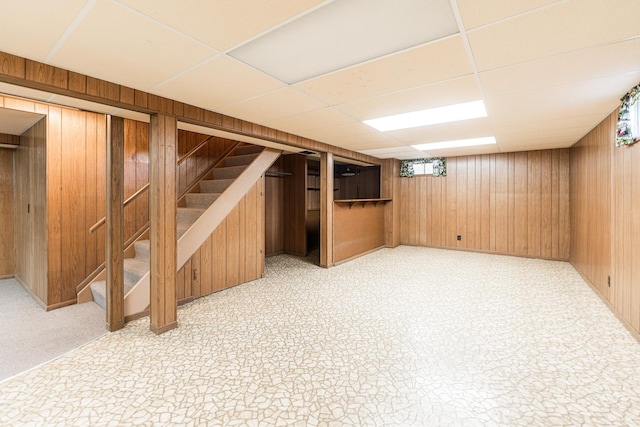 finished basement with light floors, wooden walls, and stairway