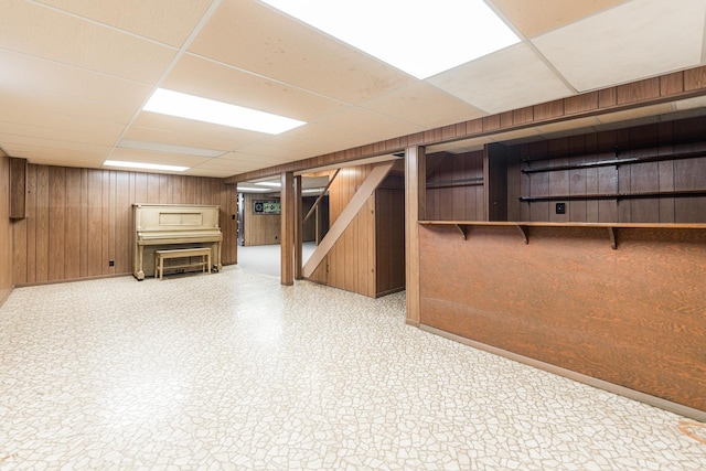 finished basement featuring a paneled ceiling, wood walls, stairs, and tile patterned floors