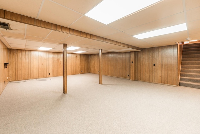 finished below grade area with carpet floors, a paneled ceiling, wood walls, and stairs