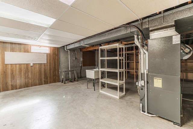 basement with heating unit, wood walls, a drop ceiling, and a sink