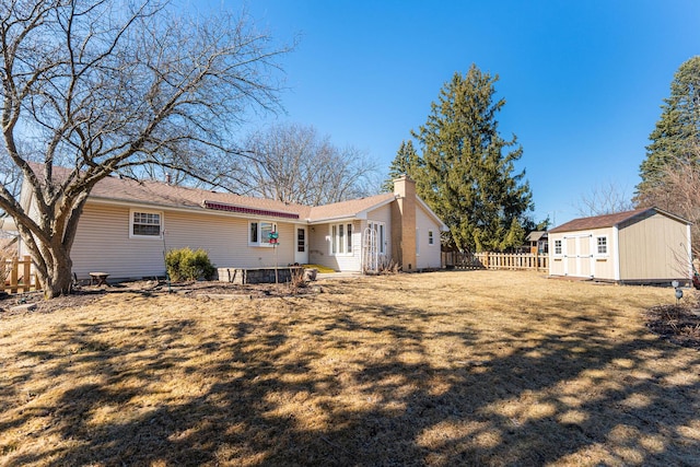 rear view of property with an outbuilding, a chimney, a lawn, a storage shed, and fence