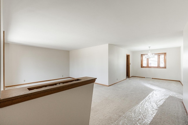 empty room with baseboards, light carpet, visible vents, and a notable chandelier