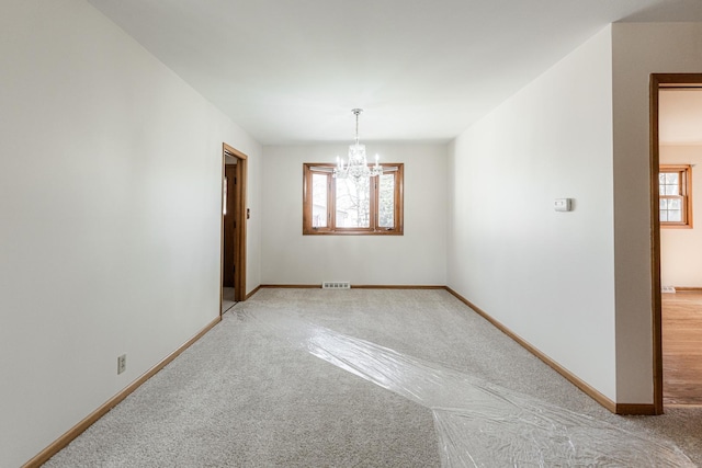 spare room featuring baseboards, plenty of natural light, visible vents, and a notable chandelier