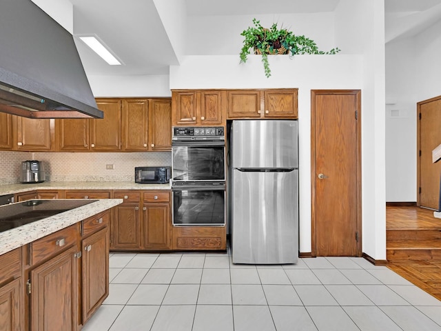 kitchen featuring tasteful backsplash, brown cabinetry, light tile patterned flooring, island range hood, and black appliances