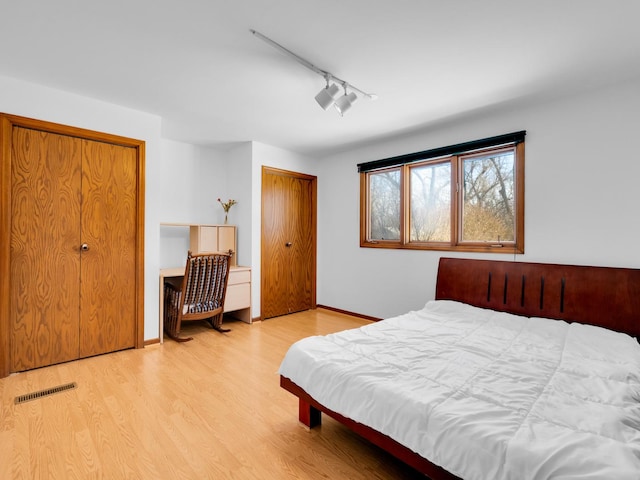 bedroom featuring visible vents, baseboards, light wood-style flooring, rail lighting, and two closets