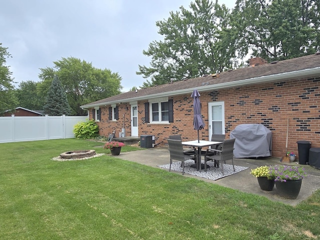 rear view of property featuring brick siding, a yard, a patio, fence, and a fire pit