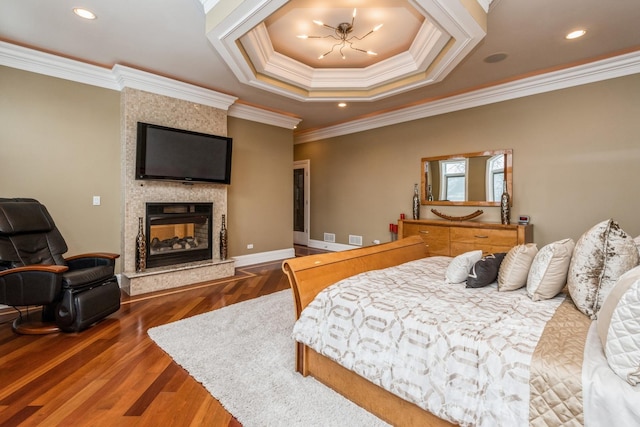 bedroom featuring wood finished floors, a tray ceiling, recessed lighting, ornamental molding, and a large fireplace