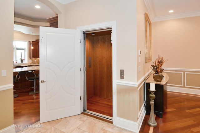 hall featuring a wainscoted wall, light wood finished floors, arched walkways, crown molding, and a decorative wall