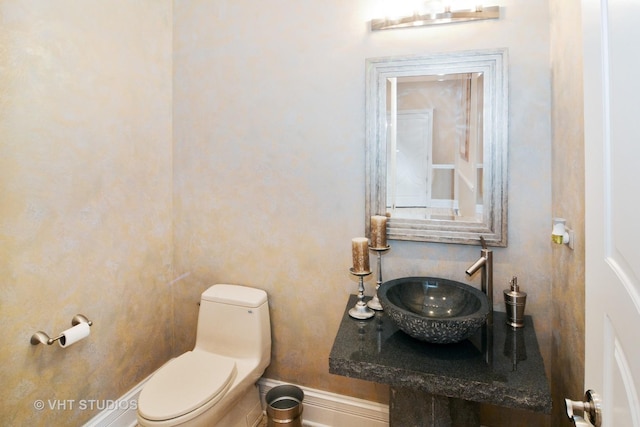 bathroom featuring toilet, baseboards, and a sink