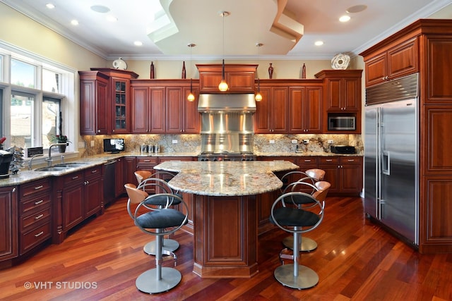 kitchen with a breakfast bar, under cabinet range hood, a sink, crown molding, and built in appliances