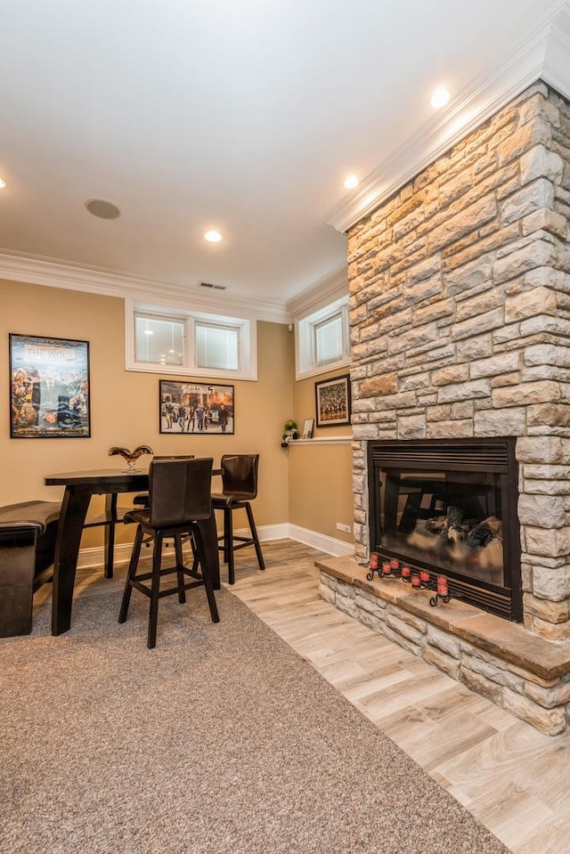 dining space with visible vents, baseboards, ornamental molding, a stone fireplace, and wood finished floors