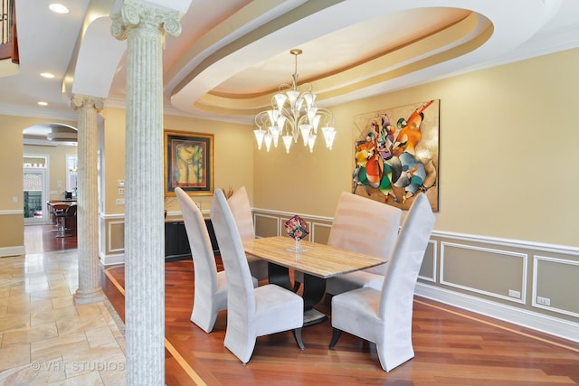 dining space featuring decorative columns, a raised ceiling, arched walkways, and crown molding