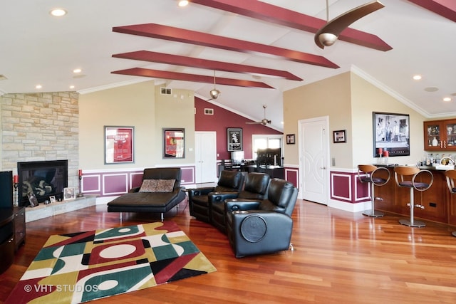 living area featuring wood finished floors, wet bar, lofted ceiling with beams, a stone fireplace, and wainscoting