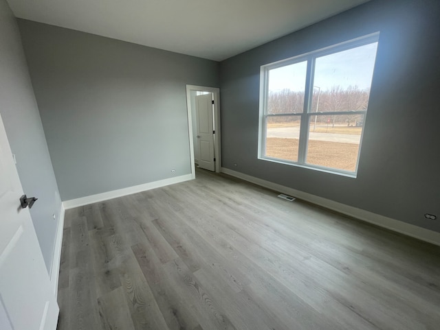 unfurnished room with visible vents, light wood-style flooring, and baseboards