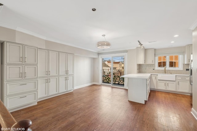 kitchen with decorative light fixtures, crown molding, light countertops, white cabinetry, and a sink