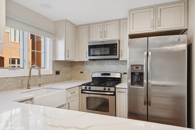 kitchen featuring stainless steel appliances, a sink, and light stone counters