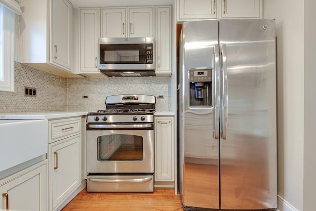 kitchen with stainless steel appliances, tasteful backsplash, light countertops, and light wood-style floors