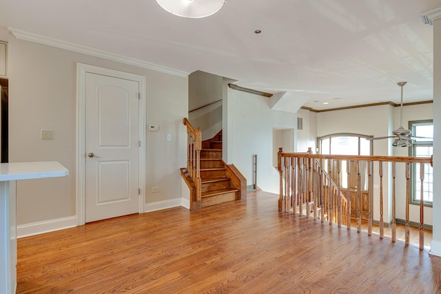 empty room with ornamental molding, light wood-type flooring, baseboards, and a ceiling fan