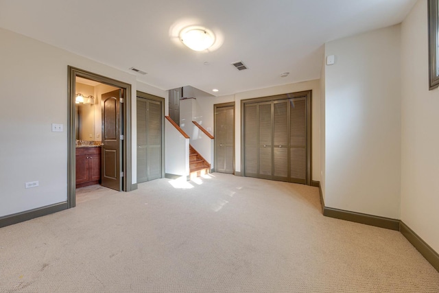 unfurnished bedroom featuring ensuite bathroom, light colored carpet, visible vents, baseboards, and multiple closets